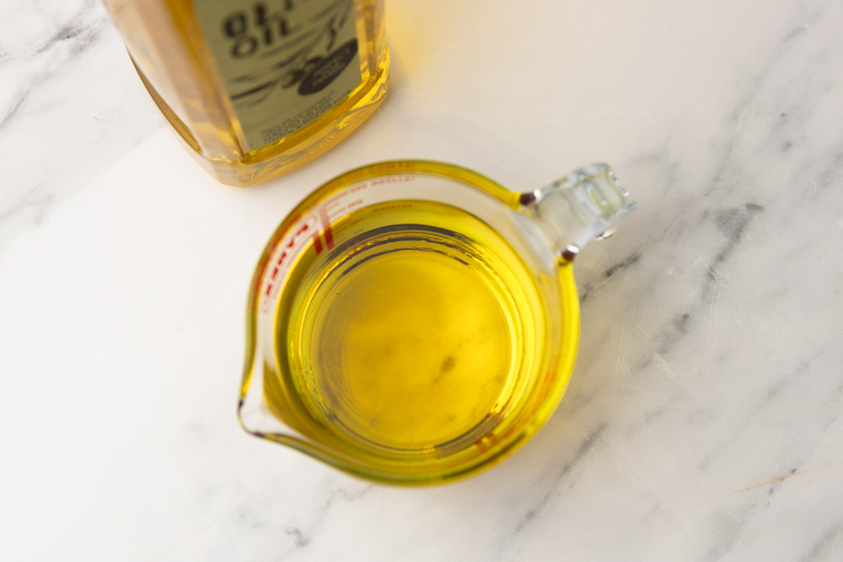 olive oil in a measuring cup placed beside a bottle of oil.