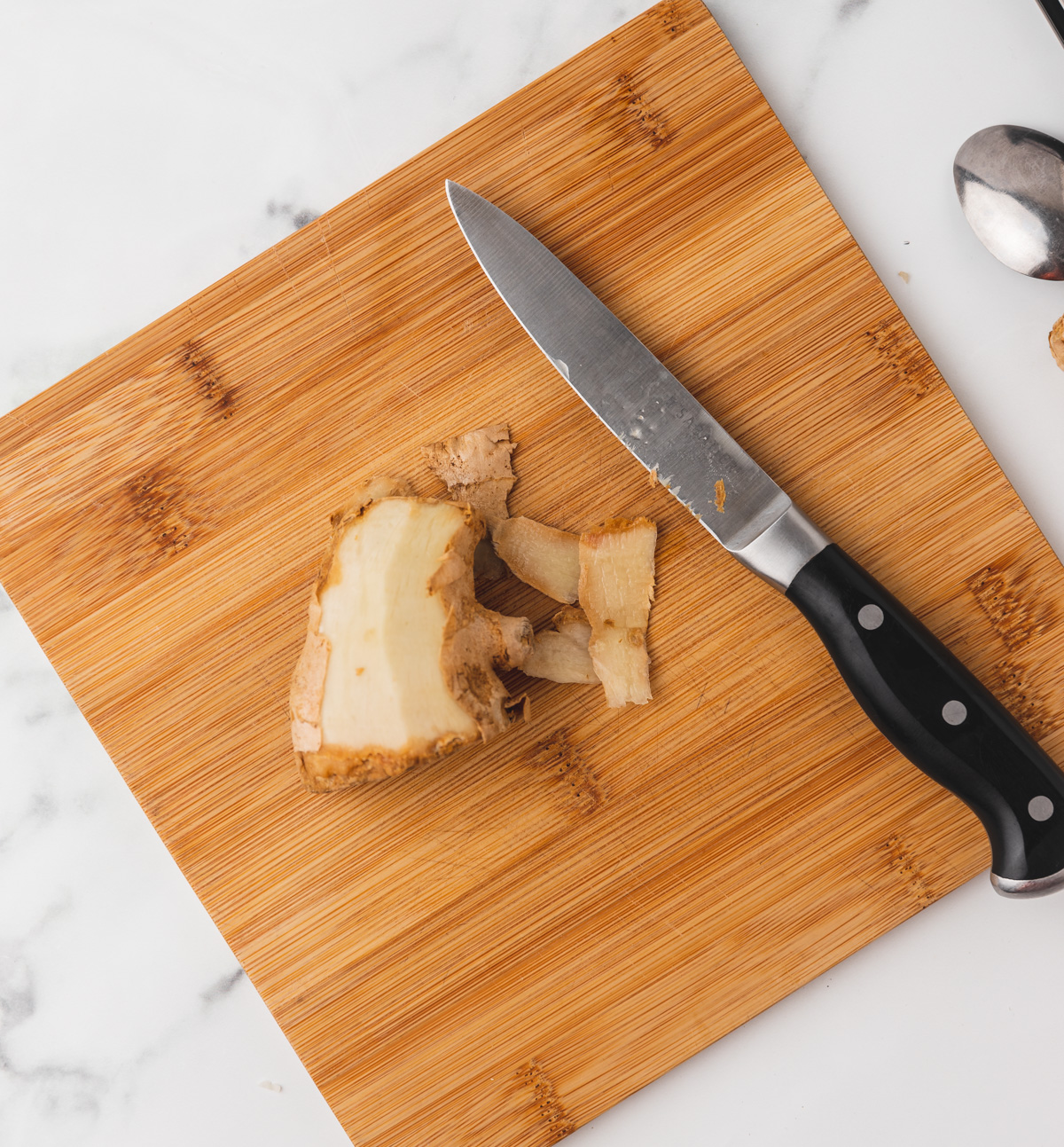 partially peeled ginger and a paring knife on a chopping board.