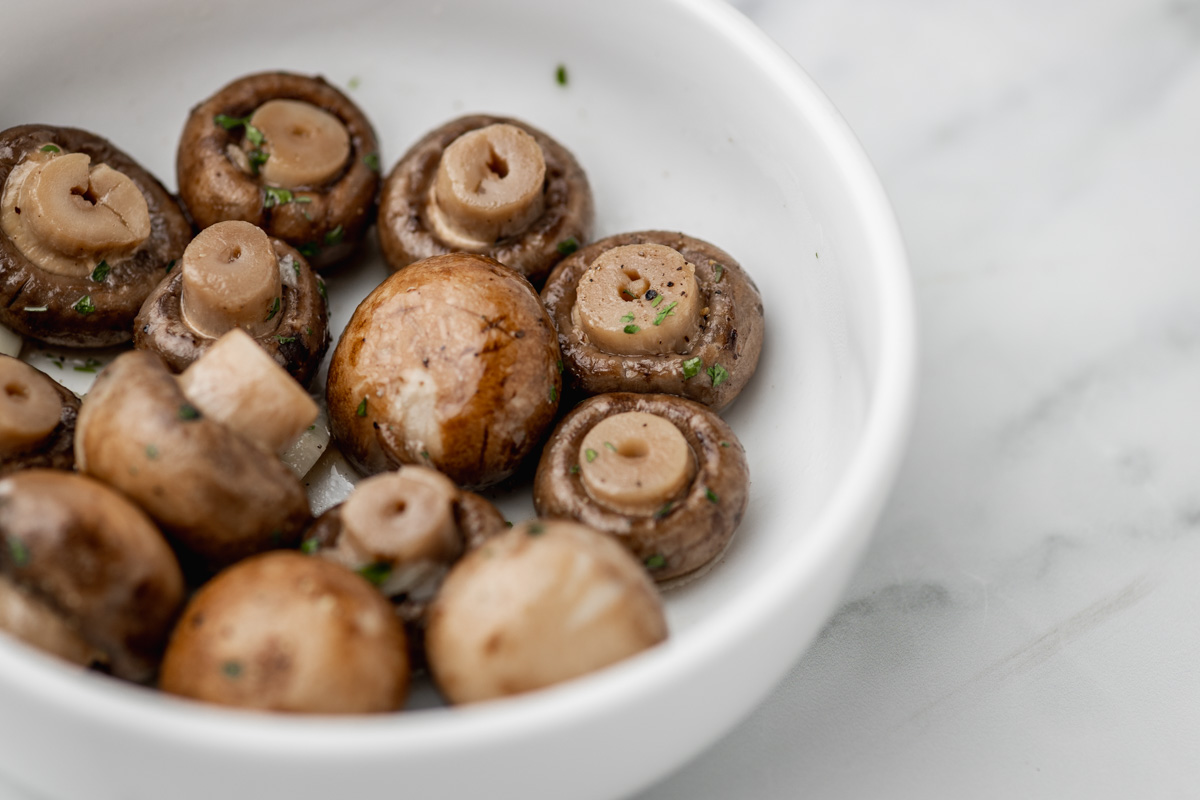 a bowl of boiled mushrooms garnished with green herbs.