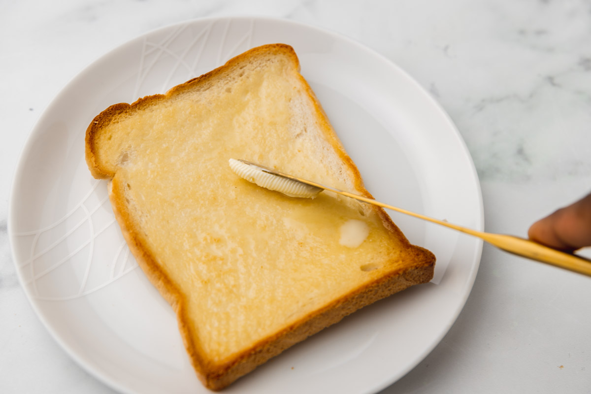 a hand spreading butter on a piece of toast.