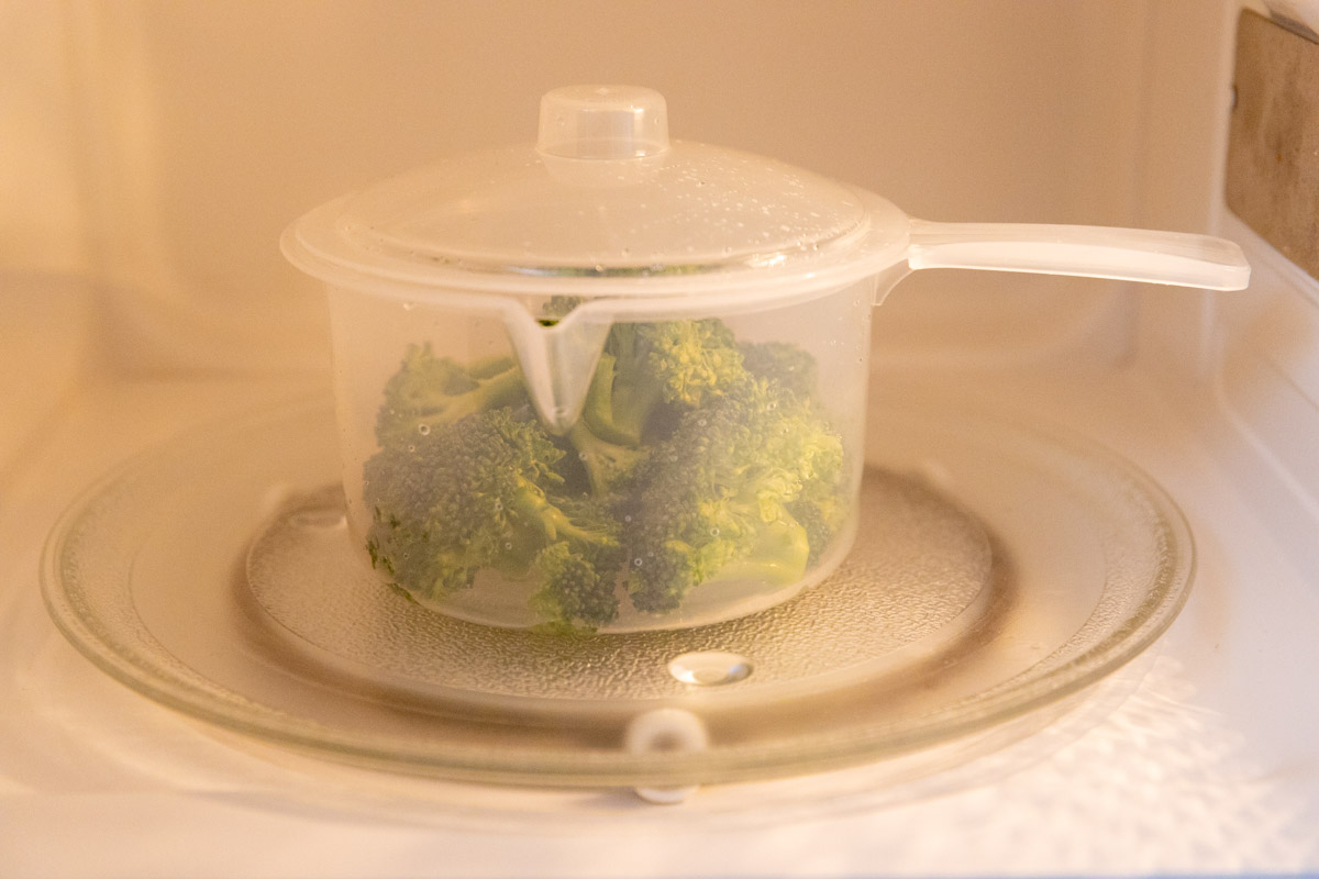 a small pot containing broccoli in the microwave.