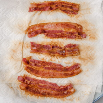 five cooked bacon pieces on a paper lined plate.