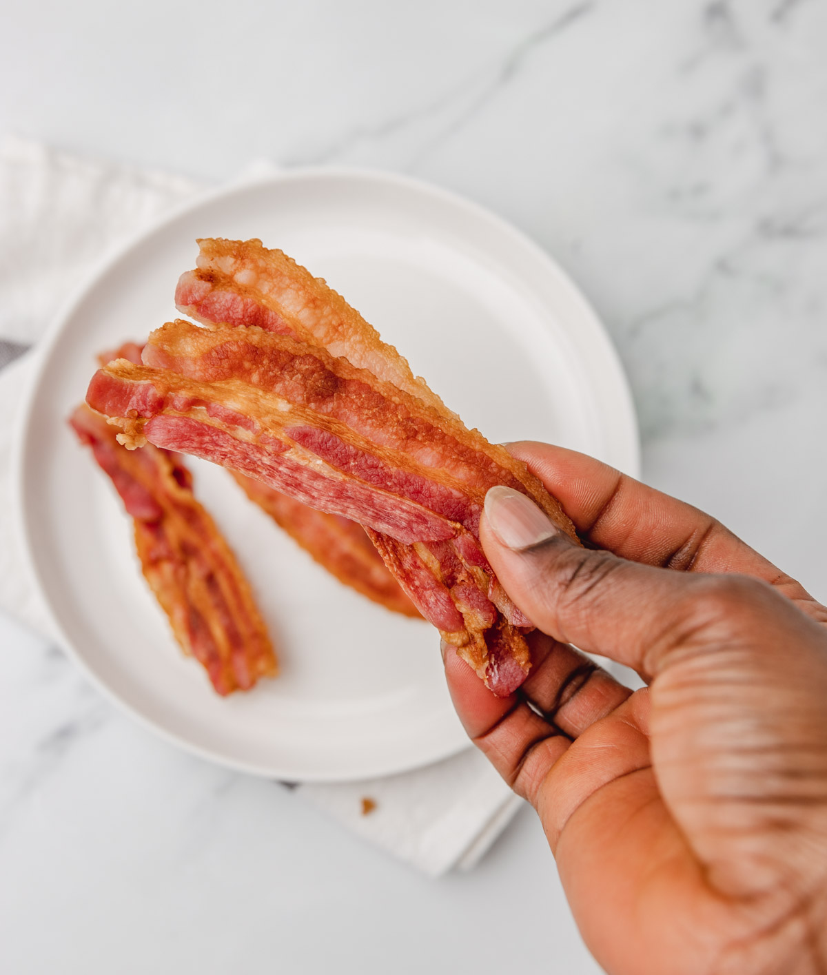 a hand holding up two crispy microwaved bacon.