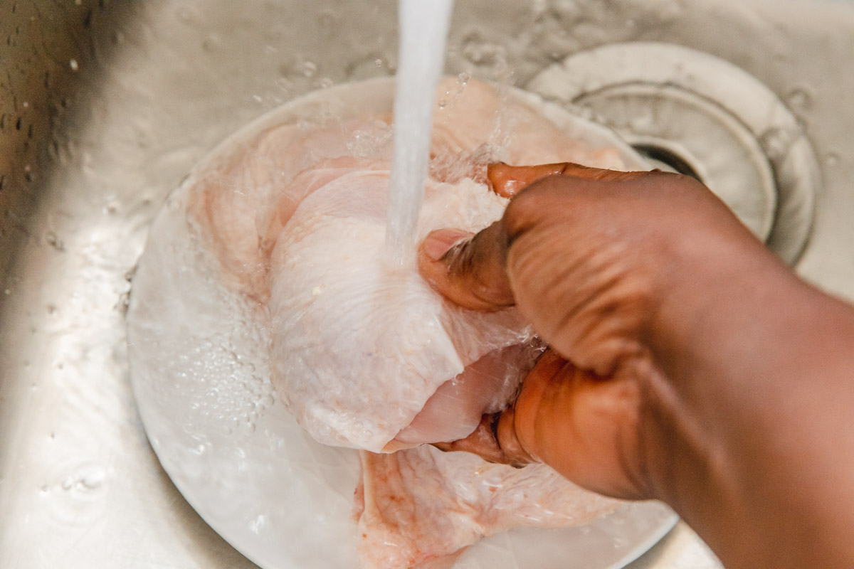 a hand holding raw chicken thigh under a tap.