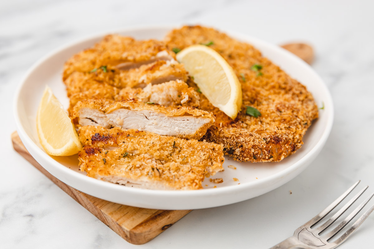 a plate of breaded chicken cutlets with lemon wedges.